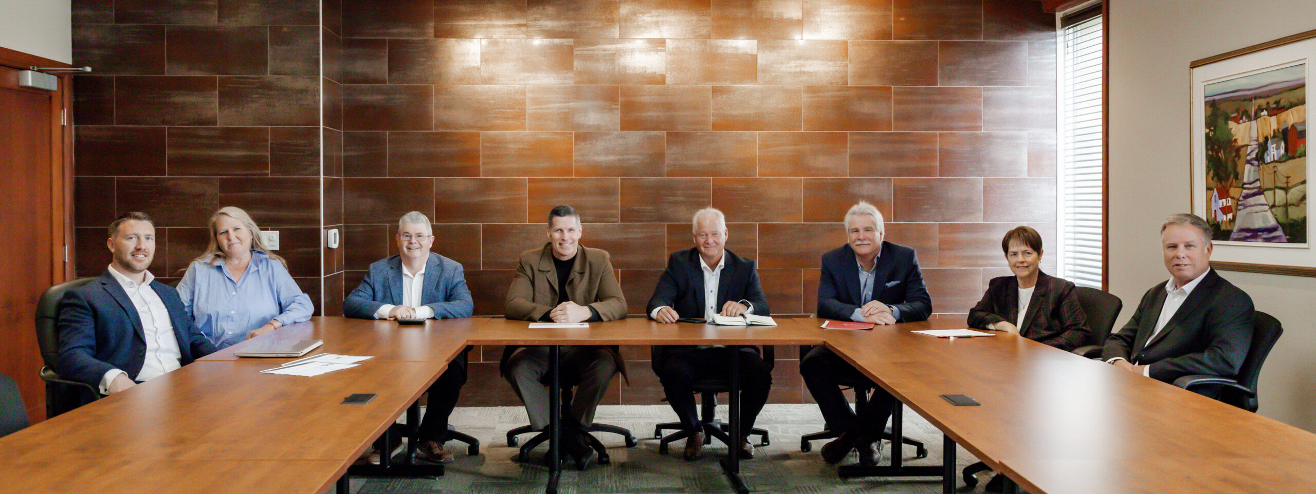 A group portrait of the Lilley Financial team sitting at a large U-shaped conference table, smiling at the camera. From left to right: Mike James, Lois Murphy, Craig Lilley, Michael Godfrey, Jim Fockens, Mark James, Patty Etling, and Philip Rayson. They are all professionally dressed in business attire.