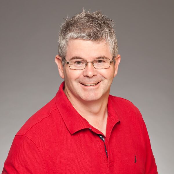 Craig Lilley smiling with short graying hair and glasses wearing a bright red polo shirt against a plain gray background